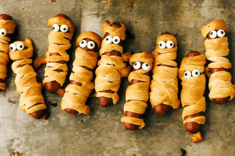 Mummy hot dogs wrapped in crescent dough with candy eyes on a baking sheet.
