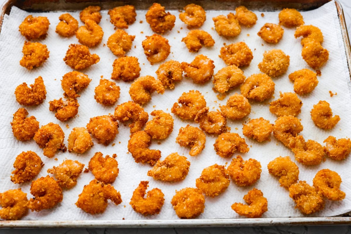 Crispy popcorn shrimp spread out on a paper towel after being fried. 