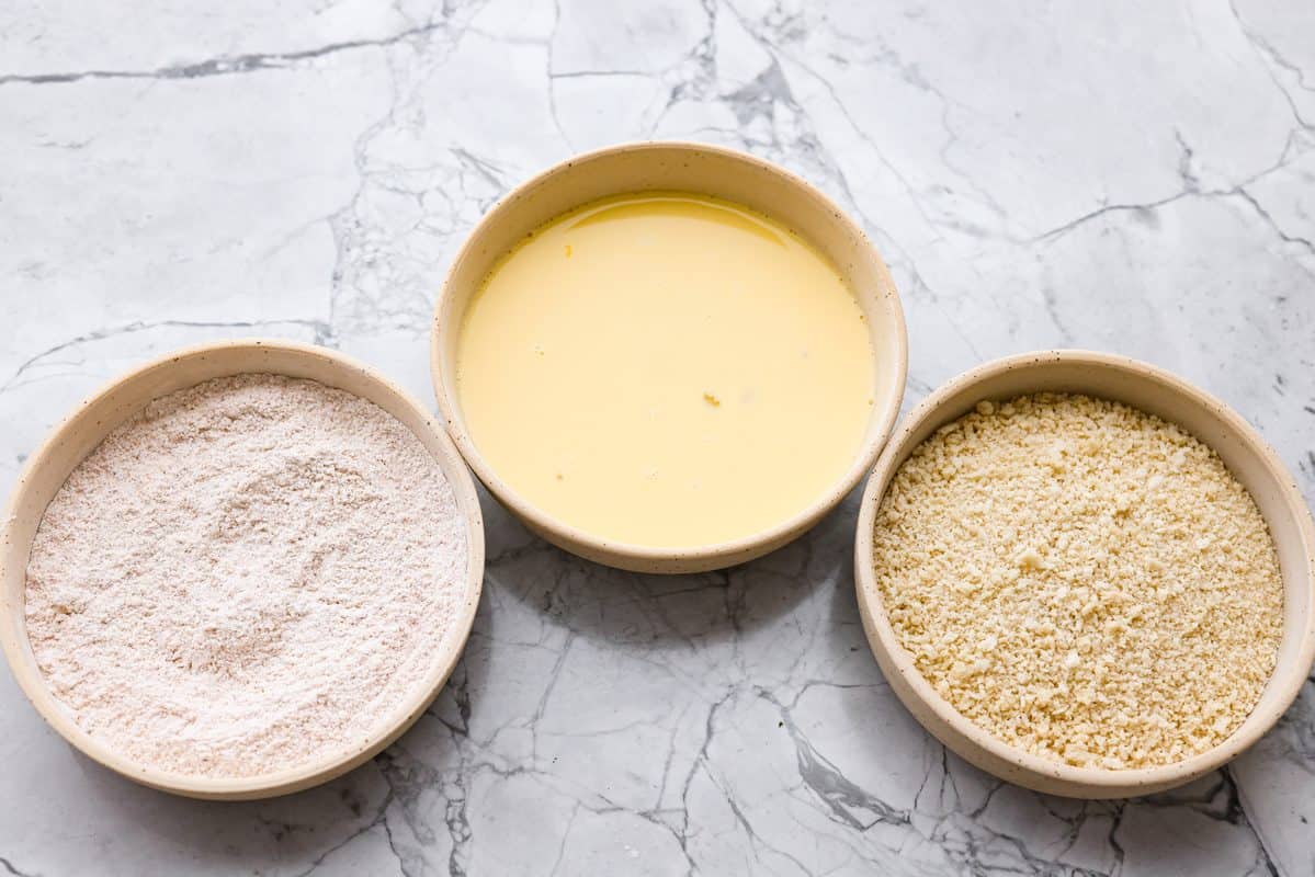 Three shallow bowls with flour mixture, egg mixture, and breadcrumb mixture in each. 