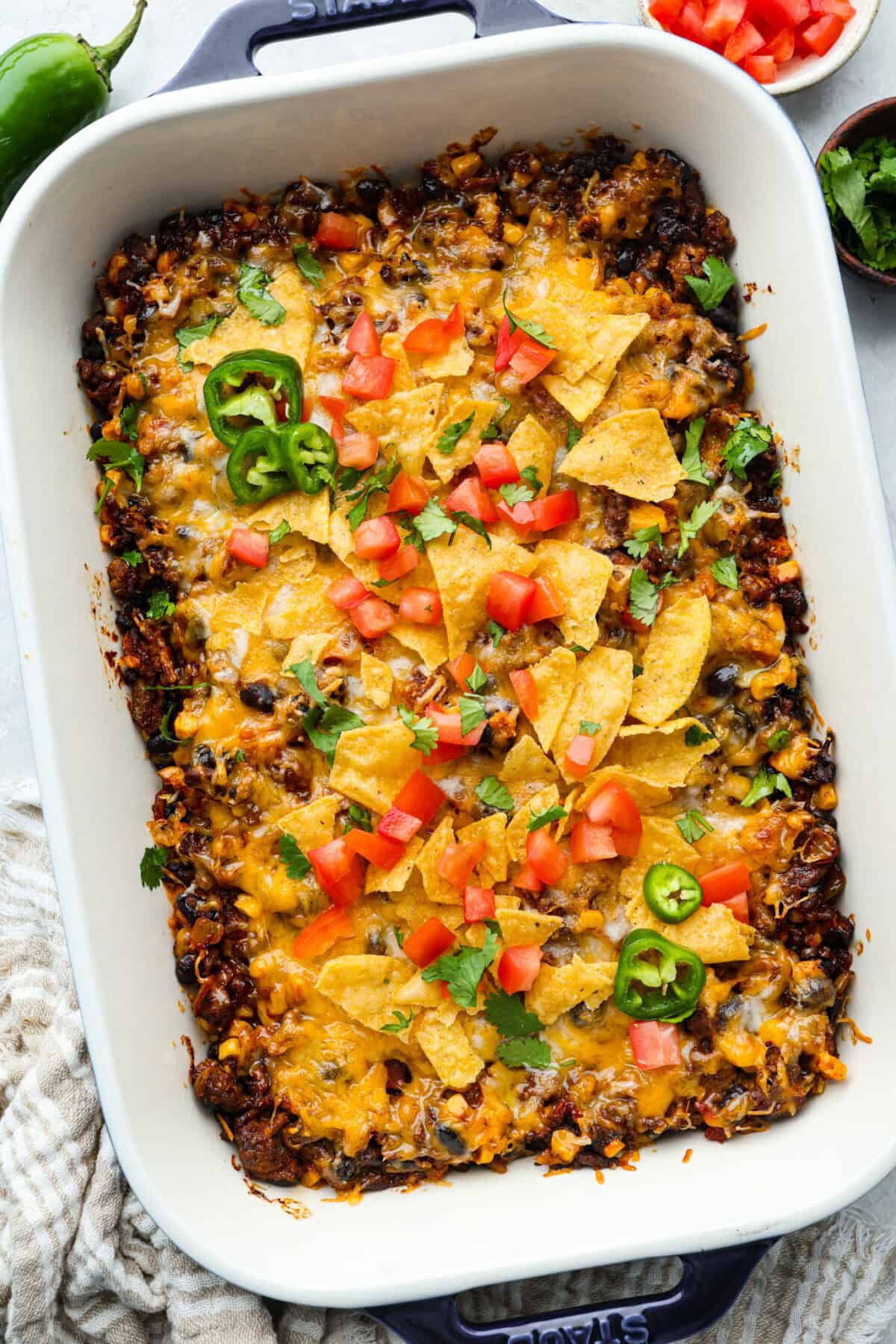 Overhead shot of baked taco casserole topped with chips, cheese, tomatoes and cilantro with a couple of slices of jalapeno. 