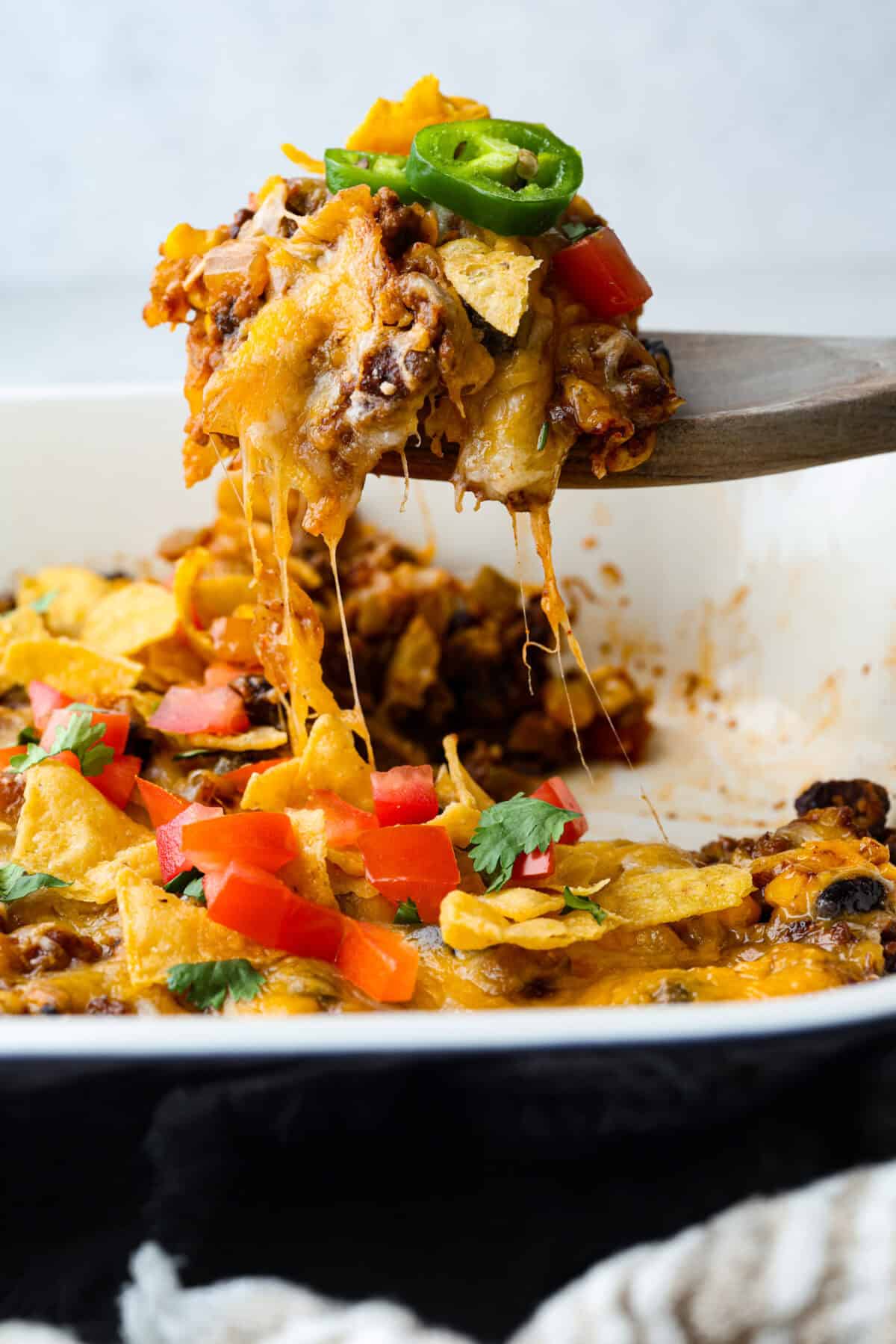 Someone scooping a serving of taco casserole out of the baking dish, with a stringy cheese pull.