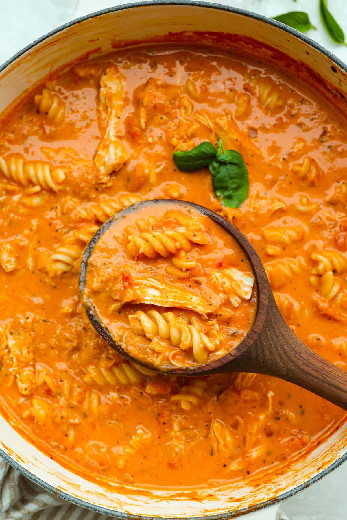 Pot of chicken parmesan soup with a wooden ladle and fresh basil leaf. 