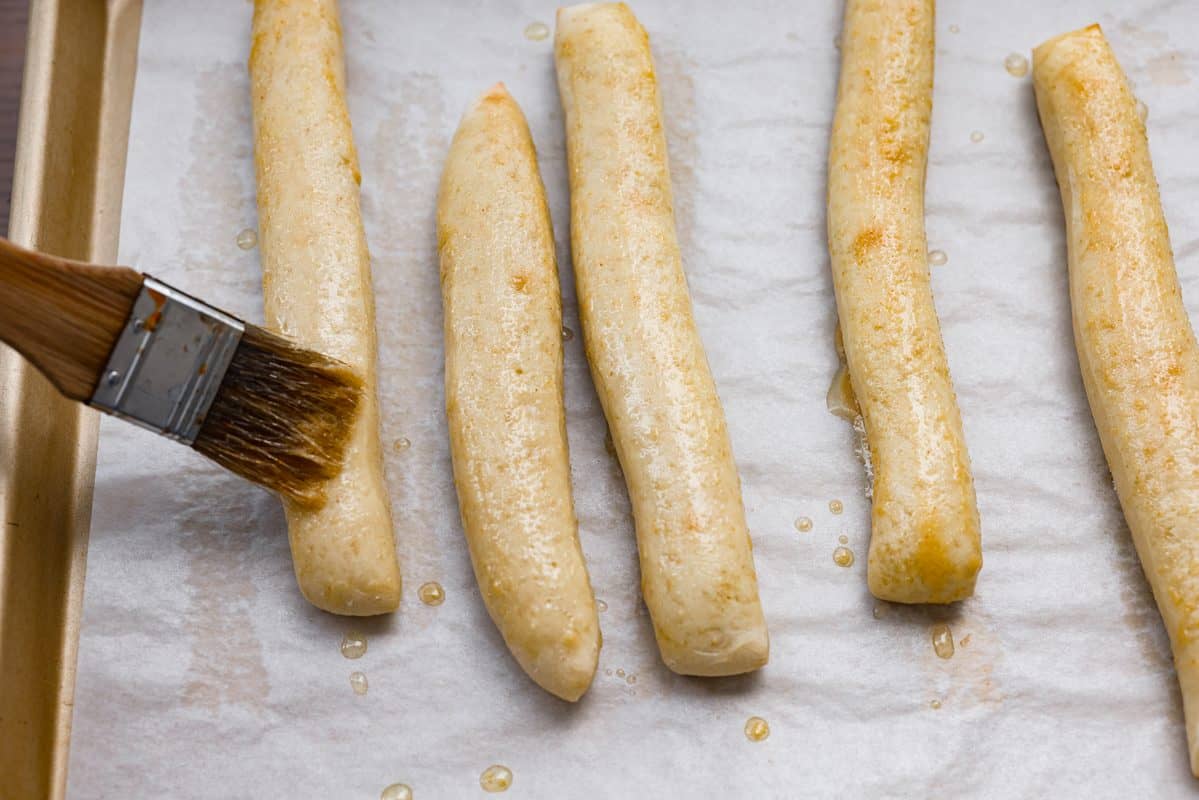 Someone spreading the melted garlic butter on a breadsticks. 