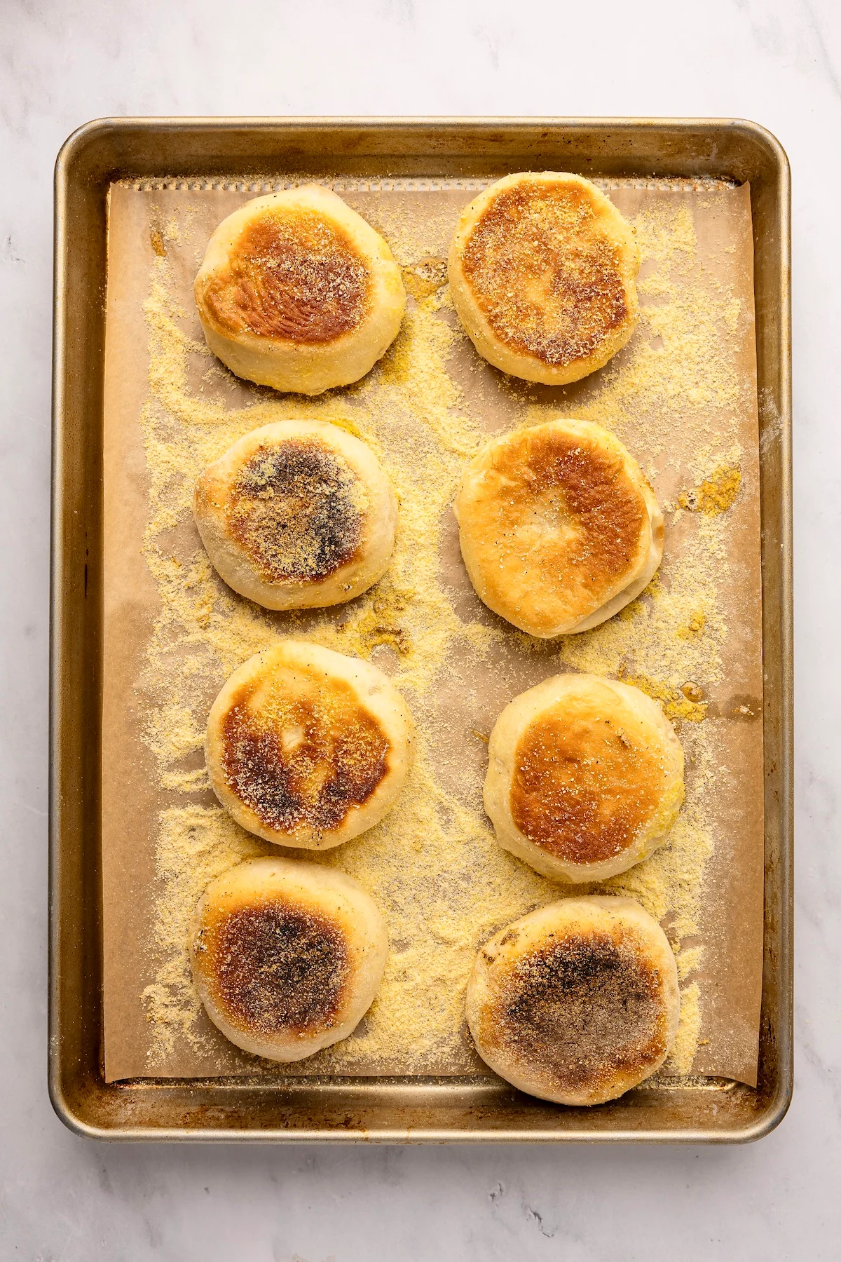 Parchment-lined baking sheet with baked English muffins