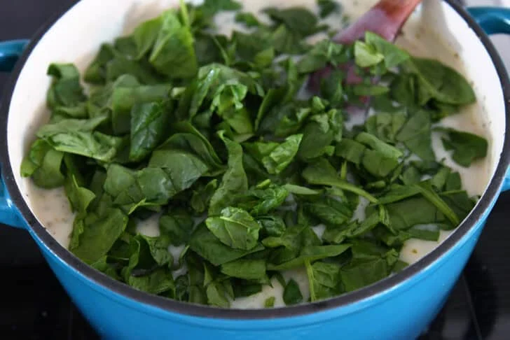 Fresh spinach added to cast iron enamel pot with gnocchi soup.
