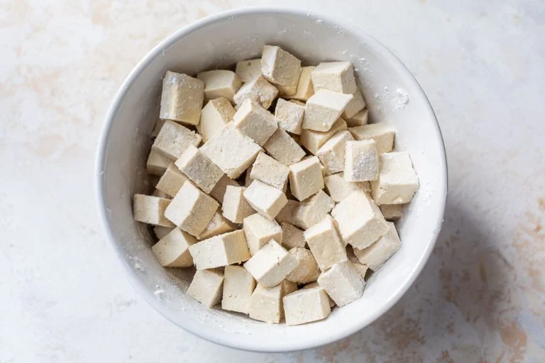A white bowl filled with cubes of raw tofu dusted with flour.