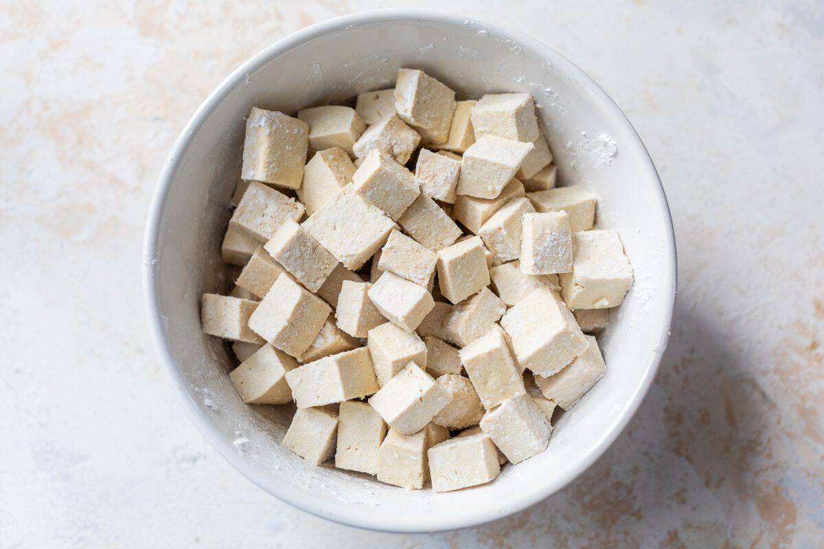 A white bowl filled with cubes of raw tofu dusted with flour.