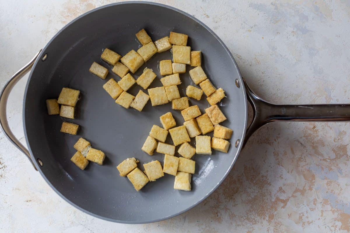 Cubes of golden-brown pan-fried tofu in a grey skillet.