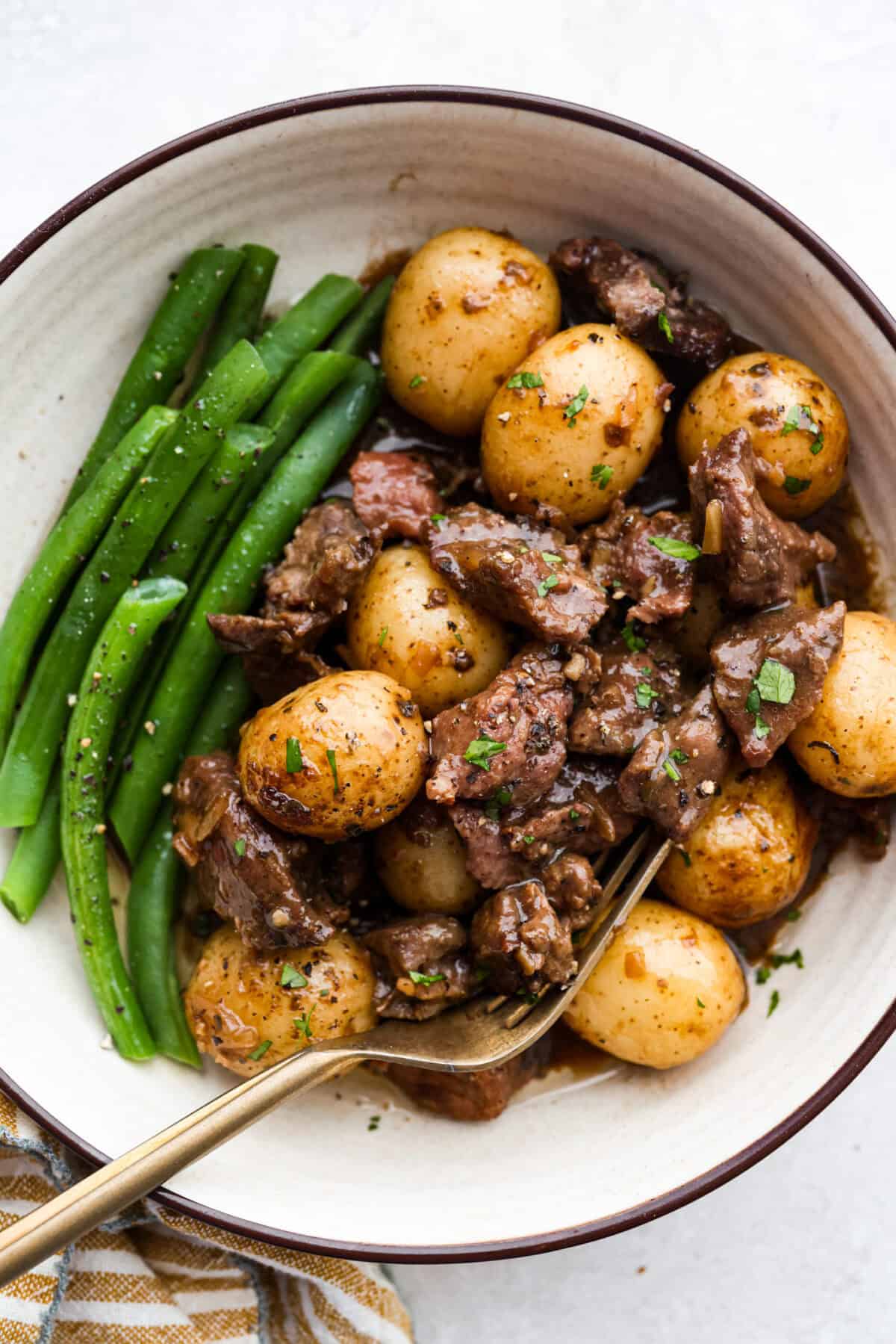 Plated green beans and slow cooker steak and potatoes garnished with fresh parsley. 