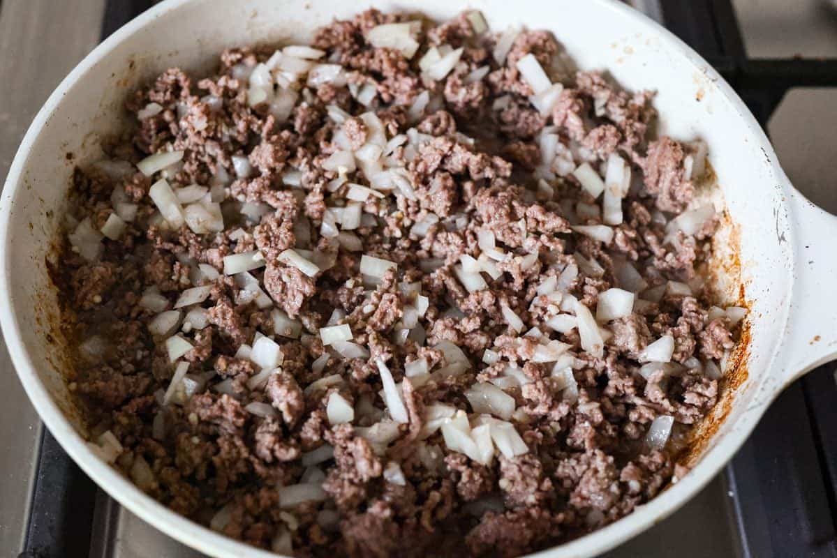 Ground beef and onions cooking in a skillet.